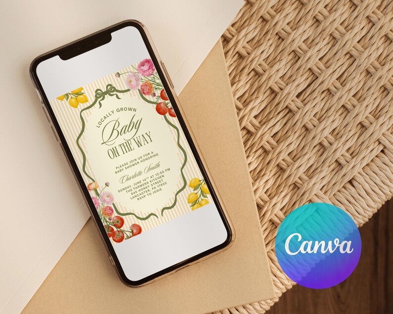 May include: A smartphone displays a baby shower invitation with floral and fruit illustrations. The invitation reads "Locally Grown Baby On The Way" with details for the event. The phone rests on a neutral surface, with a Canva logo in the corner.