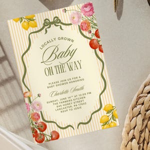 May include: Baby shower invitation with a cream background and vertical yellow stripes. The text reads "Locally Grown Baby On The Way." Floral and fruit illustrations, including lemons, tomatoes, and roses, decorate the border. The invitation includes the date, time, and location.
