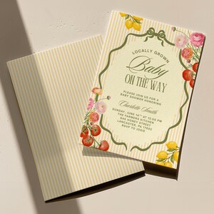 May include: Baby shower invitation with the text "Locally Grown Baby On The Way." The invitation has a cream background with vertical stripes and is decorated with watercolor lemons, tomatoes, and flowers. The invitation includes the date, time, and location.
