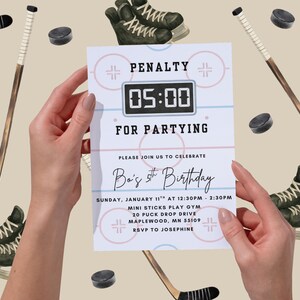 May include: A hockey-themed birthday invitation held by hands. The invitation reads "PENALTY FOR PARTYING" with a digital clock graphic showing "05:00". The invitation also includes party details, hockey sticks, skates, and pucks.