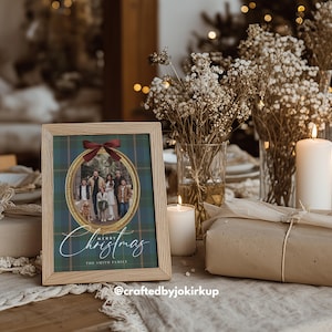 May include: A framed family photo with a Christmas theme. The photo is in an oval shape, surrounded by a gold border and a red bow. The words "Merry Christmas" are written in elegant script below the photo. The frame is made of light wood.