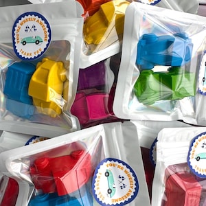 May include: Multiple clear plastic pouches containing colorful car-shaped crayons in red, blue, yellow, green, and purple. Each pouch features a round sticker with a light blue car illustration and the text You're Wheely Awesome Thank You.