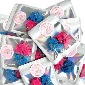 May include: A collection of small, holographic, resealable pouches, each containing two unicorn-shaped wax melts in bright pink and blue with gold glitter accents. Each pouch features a round sticker with a unicorn and the text You're One of a Kind Thank You.