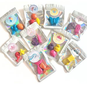Puede incluir: Surtido de pequeños derretidos de cera de colores en bolsas transparentes. Las formas incluyen una mariposa, helado, pelotas deportivas, un unicornio, una cola de sirena, un pulpo y un coche. Cada bolsa tiene una pegatina decorativa.