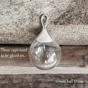 May include: A clear glass ball with a silver cap. The cap has a loop on top. The text "These caps need to be glued on." is visible below the ball. The text "20mm ball D cap" is visible below the ball.