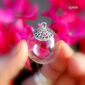 Op de afbeelding: Een transparante glazen globe hanger met een zilveren filigraan bovenkant en een lus om op te hangen. De globe heeft een diameter van 25 mm.