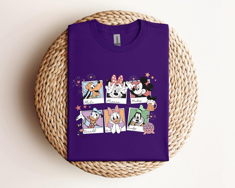 May include: A purple crew neck t-shirt featuring a graphic print of six polaroid-style frames. Each frame contains a different Disney character: Pluto, Minnie Mouse, Mickey Mouse, Donald Duck, Daisy Duck, and Goofy, with their names written below.