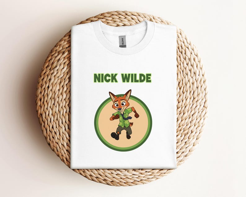 May include: White t-shirt featuring a cartoon image of Nick Wilde from Zootopia. The design includes the character's image inside a green circle, with the name "NICK WILDE" printed above in green letters. The shirt is folded on a woven, light brown surface.
