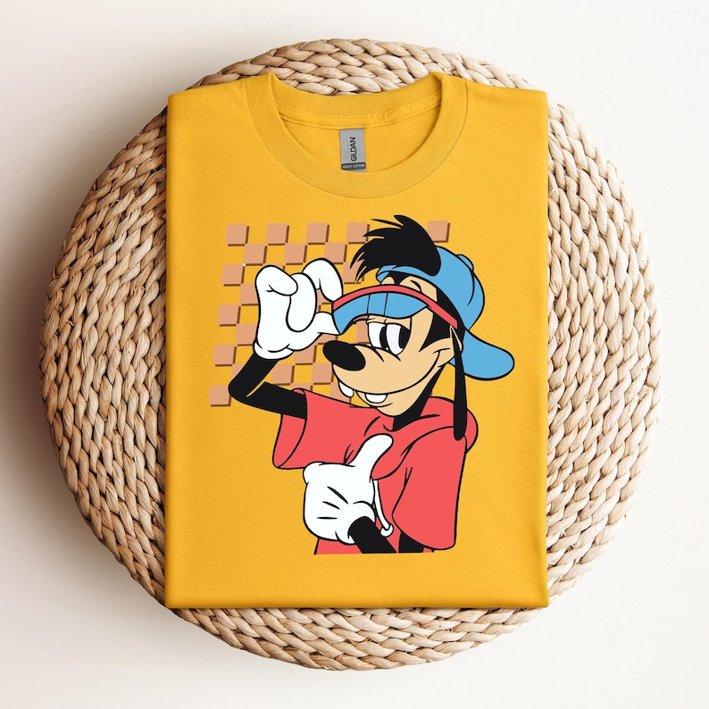 May include: A yellow t-shirt with a cartoon image of Goofy wearing a blue baseball cap, sunglasses, and a red shirt. The background is a checkered pattern.