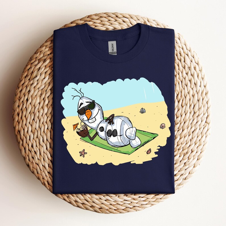 Op de afbeelding: Een marineblauw t-shirt met een cartoonillustratie van Olaf uit Frozen, die een zonnebril draagt en ontspant op een strandhanddoek met een kokosnootdrankje.