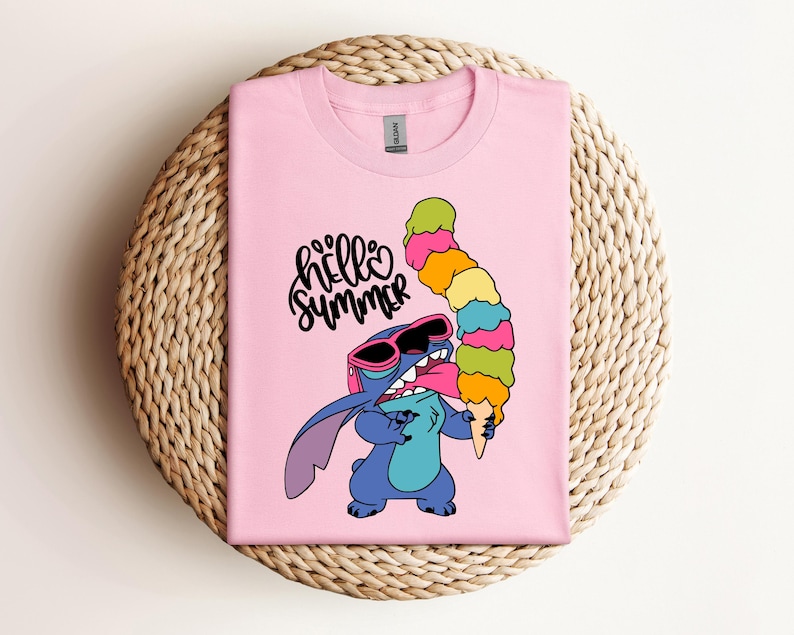 May include: A light pink t-shirt featuring a cartoon character wearing sunglasses and holding a colorful ice cream cone. The text "hello summer" is written above the character in black script.