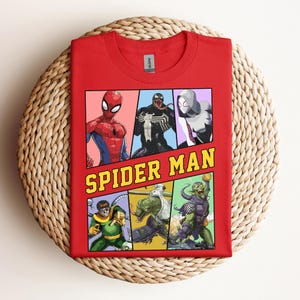 Pode incluir: Camiseta vermelha com um gr&aacute;fico de quadrinhos do Homem-Aranha e outros personagens. O gr&aacute;fico &eacute; dividido em pain&eacute;is com as palavras "SPIDER MAN" em letras amarelas. A camiseta est&aacute; dobrada em uma superf&iacute;cie tecida.