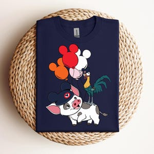 Op de afbeelding: Marineblauw T-shirt met een cartoon illustratie van een varken met een hoed, een haan en ballonnen in rood, oranje, roze en wit. Het varken heeft een zwarte hoed met een rode cirkel. De haan is groen, geel en blauw.