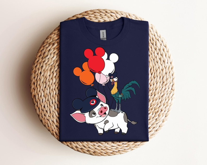 Op de afbeelding: Marineblauw T-shirt met een cartoon illustratie van een varken met een hoed, een haan en ballonnen in rood, oranje, roze en wit. Het varken heeft een zwarte hoed met een rode cirkel. De haan is groen, geel en blauw.