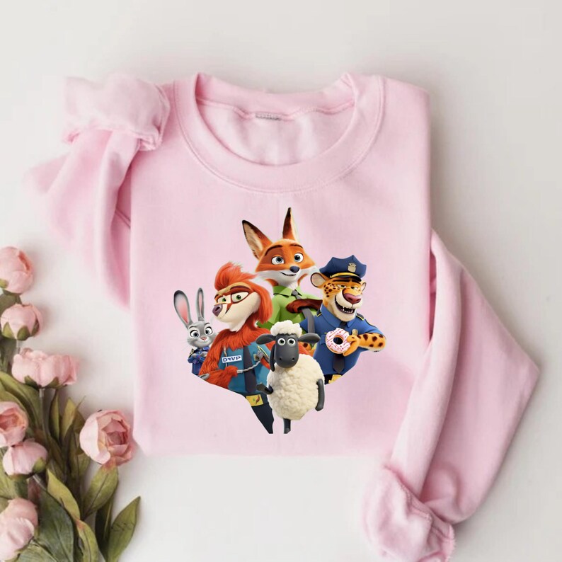 Op de afbeelding: Een lichtroze sweatshirt met een afbeelding van personages uit de animatiefilm Zootopia. De personages zijn een vos, een konijn, een schaap en een cheetah. De sweatshirt heeft lange mouwen en een ronde hals.