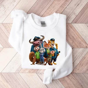 Puede incluir: Sudadera blanca de cuello redondo con un gr&aacute;fico colorido de personajes de la pel&iacute;cula animada Zootopia. El dise&ntilde;o incluye una ardilla, un conejo, un zorro, un guepardo y un b&uacute;falo de agua, todos con uniformes de polic&iacute;a. La sudadera est&aacute; hecha de un material suave.