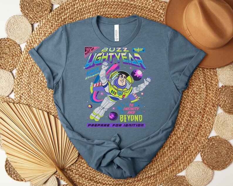 Puede incluir: Una camiseta azul con un dise&ntilde;o de Buzz Lightyear. El dise&ntilde;o incluye el texto "Buzz Lightyear" en una fuente retro colorida, junto con la frase "&iexcl;Hasta el infinito y m&aacute;s all&aacute;!".