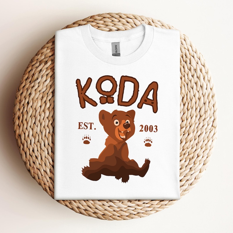 May include: White t-shirt with a brown bear cartoon illustration and the text "KODA EST. 2003".