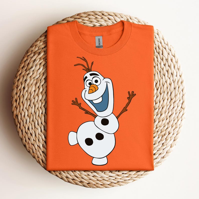Pode incluir: Camiseta laranja com uma imagem de desenho animado de Olaf, o boneco de neve do filme Frozen. Olaf est&aacute; sorrindo com os bra&ccedil;os estendidos e tem um nariz de cenoura.