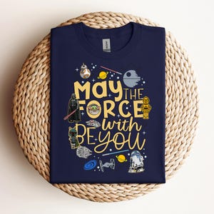 Puede incluir: Camiseta azul marino con personajes de Star Wars y la frase "May the Force be with you". El diseño incluye ilustraciones de Darth Vader, R2-D2 y otros personajes icónicos de la franquicia Star Wars.