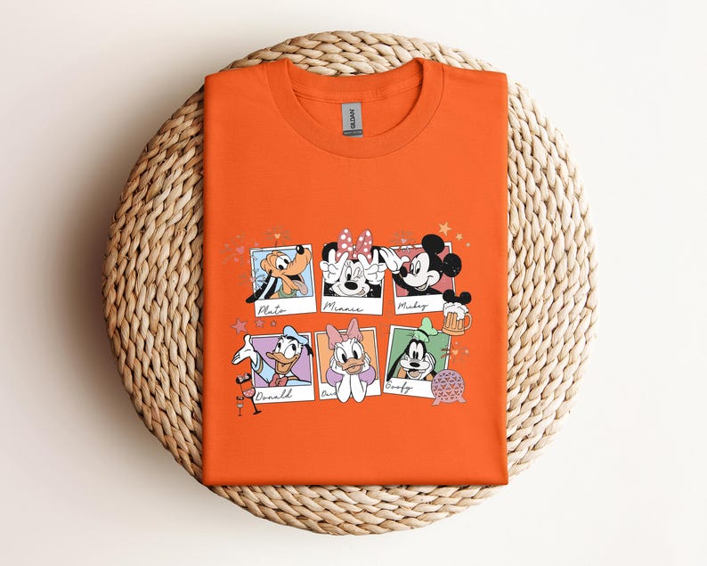 May include: An orange crew neck t-shirt featuring a graphic print of six individual polaroid-style frames. Each frame contains a different Disney character illustration with their name written below, including Pluto, Minnie, Mickey, Donald, Daisy, and Goofy.