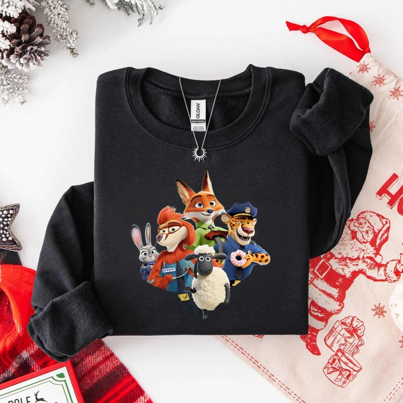 Op de afbeelding: Zwarte crewneck sweatshirt met een kleurrijke afbeelding van personages uit de animatiefilm Zootopia. Het ontwerp bevat een vos, konijn, schaap en andere personages. Een zilveren ketting is zichtbaar.