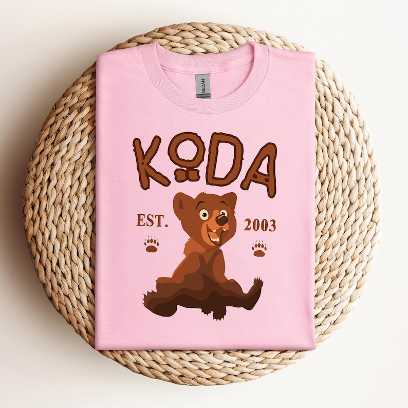 May include: Pink t-shirt with a brown bear cartoon and the text "KODA EST. 2003".
