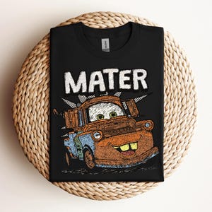 May include: Black t-shirt featuring a distressed graphic of Mater from the movie Cars. The word "MATER" is printed above the character in a bold, white font. The graphic includes shades of brown, blue, and orange.