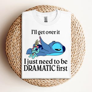 Puede incluir: Camiseta blanca con un personaje azul de Stitch de Lilo & Stitch acostado con una peque&ntilde;a mu&ntilde;eca. El texto en la camiseta dice "I'll get over it I just need to be DRAMATIC first."