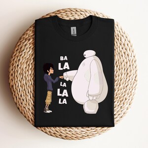 K&ouml;nnte beinhalten: Schwarzes T-Shirt mit einem wei&szlig;en Roboter und einer Comicfigur mit dem Text "BA LA LA LA LA" darauf.