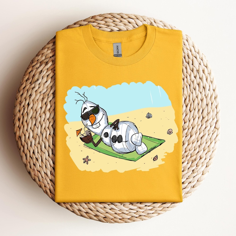 Op de afbeelding: Een geel T-shirt met een cartoon afbeelding van Olaf uit Frozen, die een zonnebril draagt en ontspant op een strandhanddoek met een kokosnootdrankje. De tekst "Let it Go" staat op het shirt gedrukt.