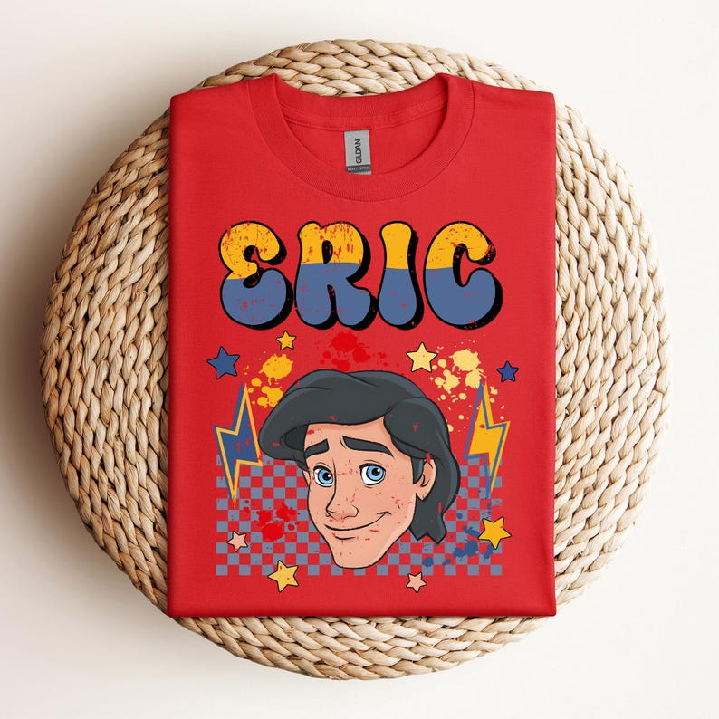 May include: Red t-shirt with the name "ERIC" in yellow and blue bubble letters. The shirt features a cartoon illustration of a man with black hair and blue eyes, along with stars, lightning bolts, and a checkered pattern.