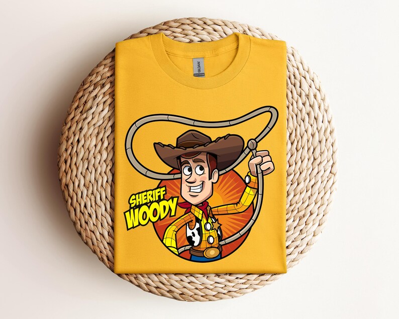May include: Mustard yellow t-shirt featuring a cartoon illustration of Sheriff Woody from Toy Story. The design includes Woody in his cowboy hat, holding a lasso, with the text "Sheriff Woody" in a yellow and white font.