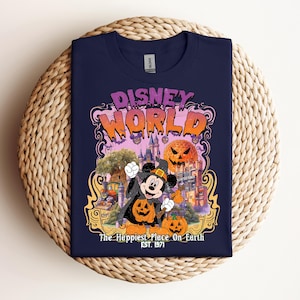 Puede incluir: Una camiseta azul marino con un estampado gráfico que incluye el texto "Disney World" y "The Happiest Place On Earth Est. 1971". El diseño muestra un ratón de dibujos animados con sombrero de bruja, una calabaza y un castillo.