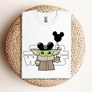 Puede incluir: Camiseta blanca con un personaje alien&iacute;gena verde que lleva un sombrero de Mickey Mouse y sostiene un globo de Mickey Mouse. El texto "Star Wars" est&aacute; impreso en la camiseta.