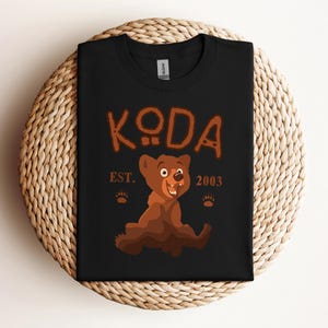 May include: Black t-shirt with a cartoon bear illustration and the text "KODA EST. 2003".