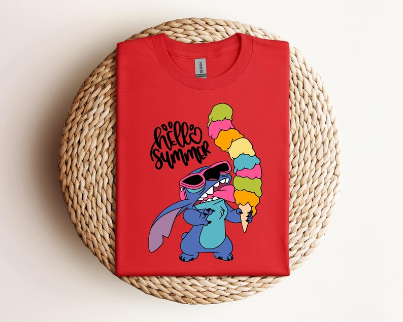 May include: Red t-shirt featuring a cartoon character wearing sunglasses and holding a large, colorful ice cream cone. The text "hello summer" is written in black script. The shirt is displayed on a woven, circular surface.