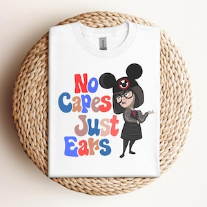 May include: White t-shirt with a cartoon character wearing a black and red Mickey Mouse hat and a black dress. The text "No capes Just Ears" is printed in colorful letters on the shirt.