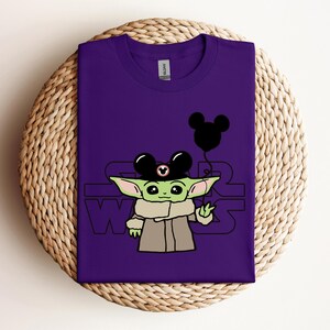 Puede incluir: Camiseta morada con un personaje verde que lleva un sombrero de Mickey Mouse y sostiene un globo de Mickey Mouse. El texto "Star Wars" est&aacute; impreso en la camiseta.