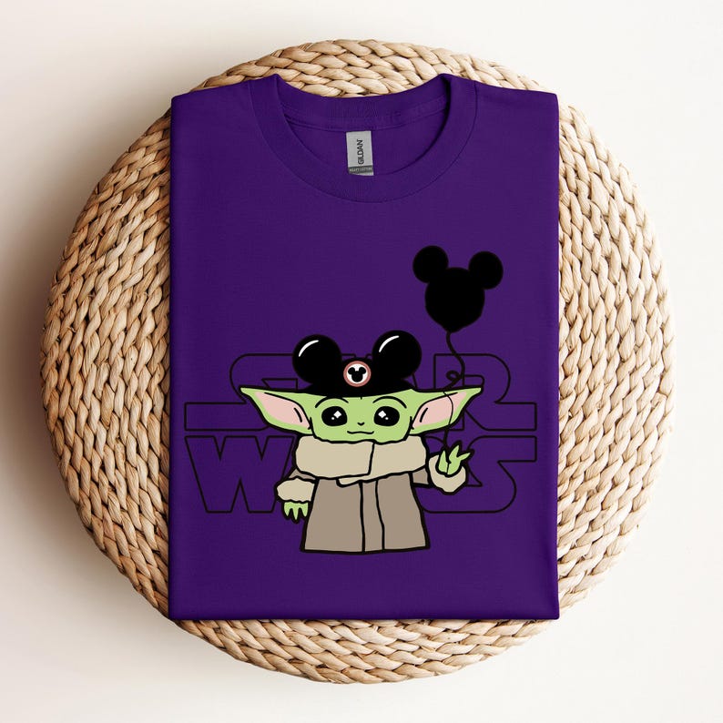 Puede incluir: Camiseta morada con un personaje verde que lleva un sombrero de Mickey Mouse y sostiene un globo de Mickey Mouse. El texto "Star Wars" est&aacute; impreso en la camiseta.