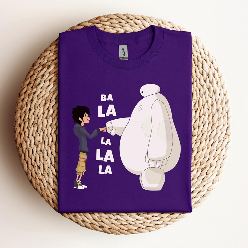 K&ouml;nnte beinhalten: Lilafarbenes T-Shirt mit einem wei&szlig;en Cartoon-Roboter und einer Jungenfigur. Der Text "BA LA LA LA" ist auf dem T-Shirt aufgedruckt.