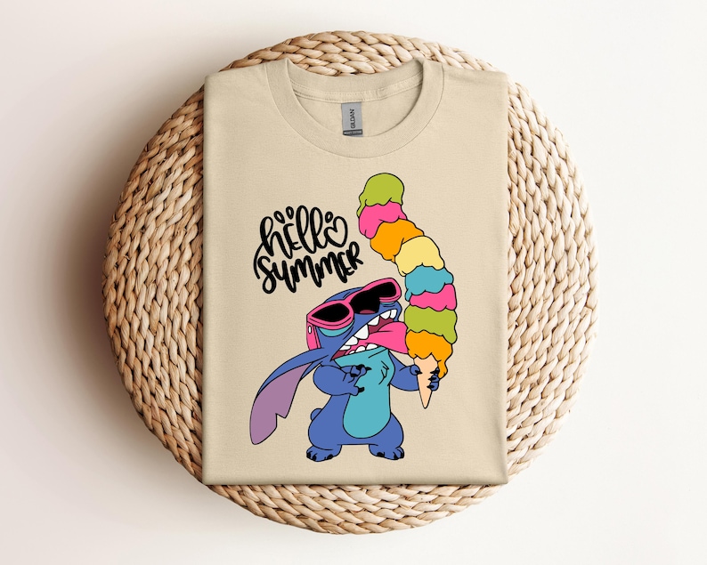May include: Beige t-shirt featuring a cartoon character wearing sunglasses and holding a tall, colorful ice cream cone. The words "hello summer" are written in a playful font above the character.