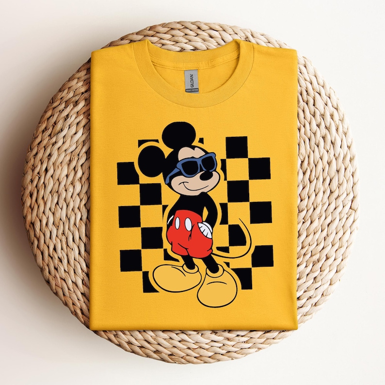 Pode incluir: Camiseta amarela com fundo xadrez preto e branco com o Mickey Mouse usando &oacute;culos de sol. O Mickey Mouse est&aacute; usando shorts vermelhos com um &uacute;nico bot&atilde;o preto.
