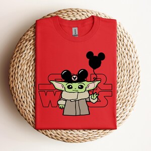 Puede incluir: Camiseta roja con un personaje verde que lleva un sombrero de Mickey Mouse y sostiene un globo de Mickey Mouse. El texto "STAR WARS" est&aacute; impreso en la camiseta.