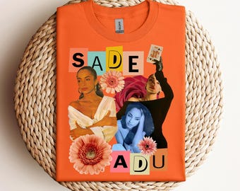 May include: Orange t-shirt featuring a collage of images of Sade Adu, with the name "SADE ADU" in colorful block letters. The design includes floral elements and a playing card.