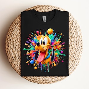 May include: Black t-shirt featuring a colorful graphic of Pluto the dog with a vibrant paint splatter design. The cartoon dog has a yellow body, black ears, and a long pink tongue. The paint splatter includes shades of blue, orange, green, and yellow.
