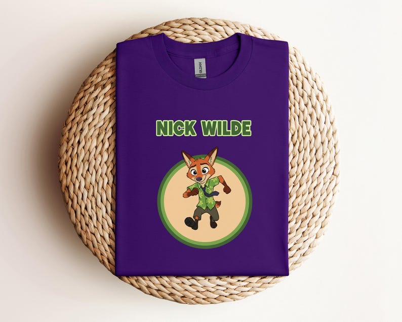 May include: A purple t-shirt featuring the text "NICK WILDE" in green letters above a cartoon image of a fox character. The fox is wearing a green shirt and tie, set within a circular design with a light green and tan border.