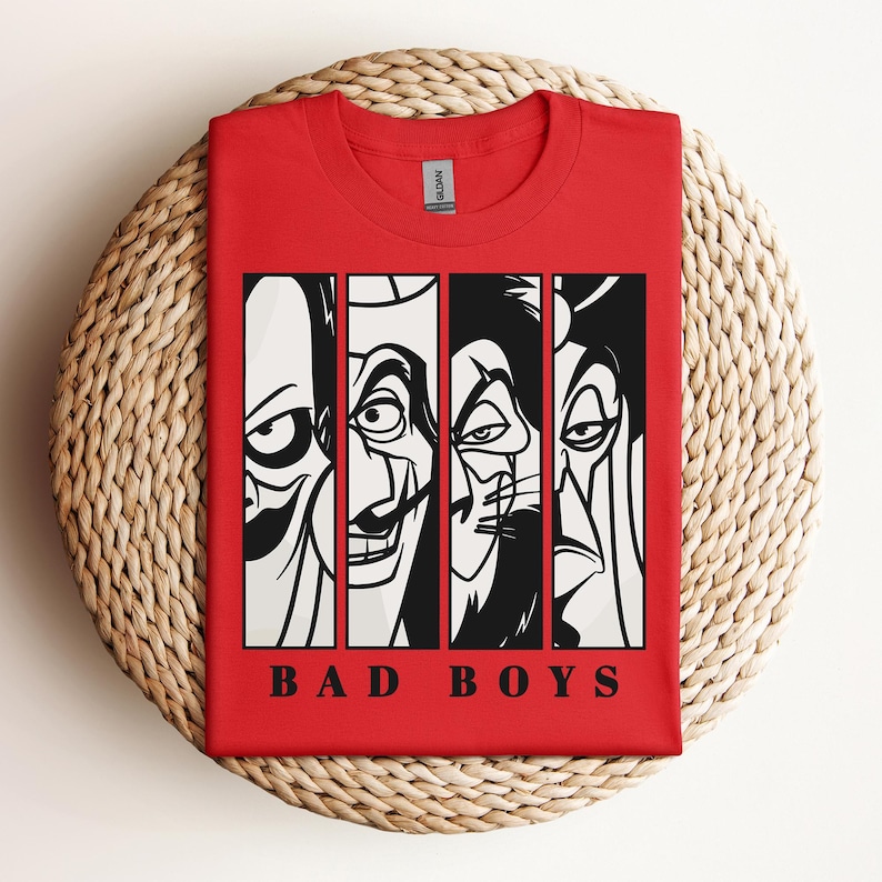 May include: A red t-shirt featuring a graphic of four cartoon villains in black and white, with the words "BAD BOYS" in a bold font at the bottom. The shirt is folded on a woven, circular surface.