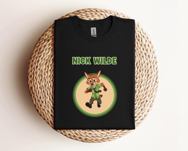 May include: Black t-shirt featuring a cartoon image of Nick Wilde from Zootopia. The design includes the character in a green and brown outfit inside a green and tan circle, with the name "NICK WILDE" above. The shirt is displayed on a woven surface.