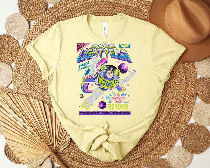 Puede incluir: Camiseta amarillo claro con un dise&ntilde;o de Buzz Lightyear. El dise&ntilde;o incluye las palabras "Buzz Lightyear" en una fuente colorida, con la frase "&iexcl;Al infinito y m&aacute;s all&aacute;!". La camiseta est&aacute; hecha de material suave.